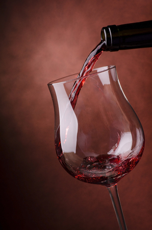 close-up of red wine poured into a glass goblet raises a splashの写真素材