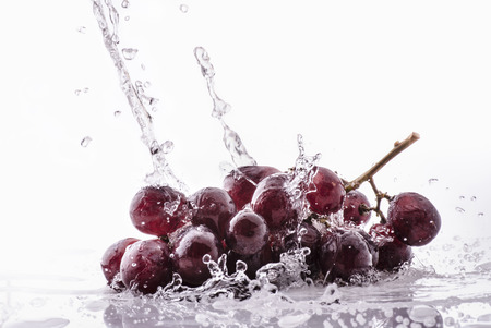 wave of clear water falls on bunch of rose grapes isolated from the white backgroundの写真素材