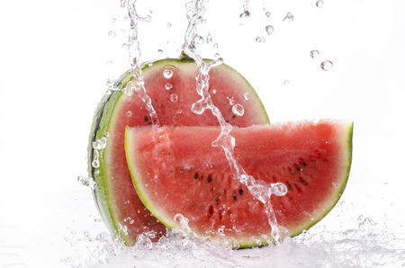 a wave of clear water falls on the sliced watermelon on a white backgroundの写真素材