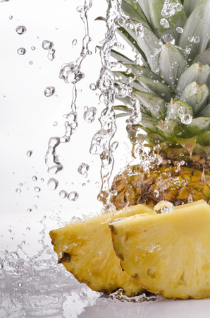 a wave of clear water falls on ripe and sliced pineapple on a white backgroundの写真素材