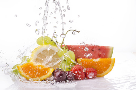a wave of clear water falling on the varied and colorful fruits on a white backgroundの写真素材