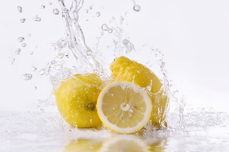 a wave of clear water falls on some lemons on a white backgroundの写真素材