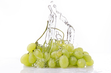 a wave of clear water falls on a cluster of white grapes on a white backgroundの写真素材