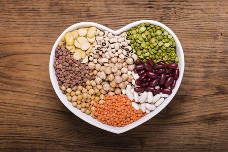 ceramic bowl in the shape of a heart full of different types of dry legumesの写真素材