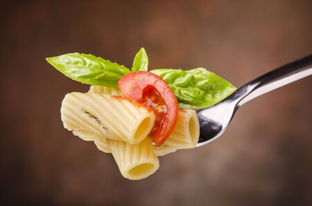closeup, fork with pasta, fresh tomato and basil leaves isolated from the background