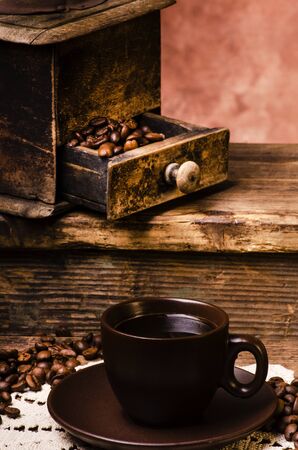 old wooden coffee grinder, cup of hot black coffee and roasted coffee beans on rustic wooden table.Still lifeの写真素材