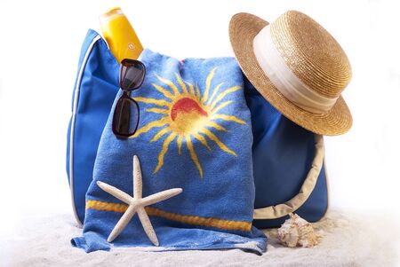 beach bag equipped with towel, sunglasses a hat and sunscreen on the coral sand and a starfish.の写真素材