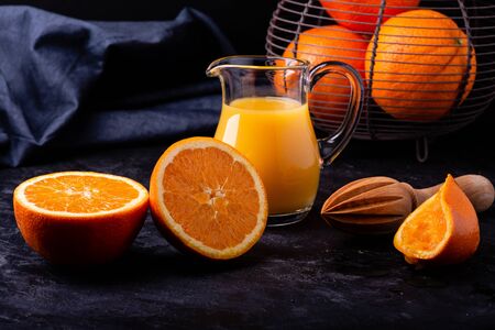 on the dark background, a carafe with freshly squeezed orange juice, a wooden citrus-fruit squeezer,...