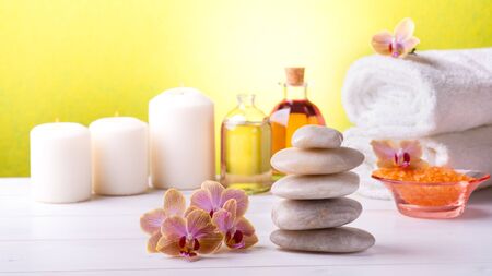 At the center of the white table are the orchids and stacked stones, in the background, white towels, bath salts, some candles and transparent bottles with perfumed essences.の写真素材
