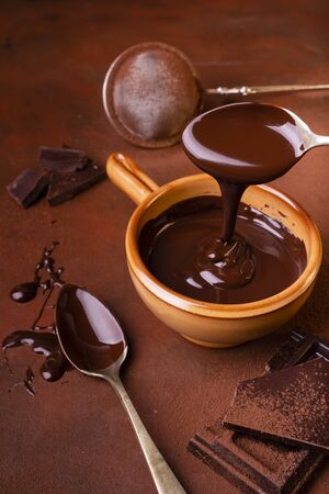 brown background, smeared with cocoa and chocolate chips, some pieces of chocolate and a bowl with melted dark chocolateの写真素材