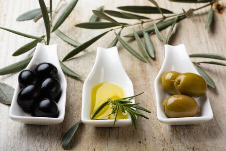 in the foreground, on the rustic wooden table, some white ceramic bowls with green and black olives and extra virgin olive oil.の写真素材