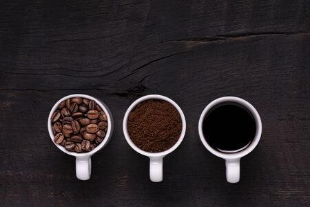 seen from above. On the dark wooden table, three cups arranged in a row contain coffee: in beans, ground and liquidの写真素材