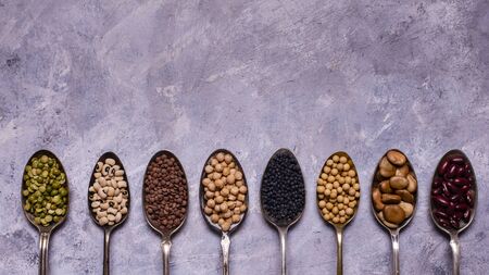 assortment of dried legumes in spoons arranged in a row with top view on a gray textured background. copy spaceの写真素材