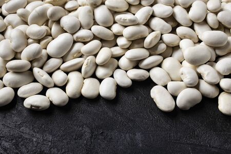 on a textured black background, in the foreground, a pile of dry and raw white beans rich in...