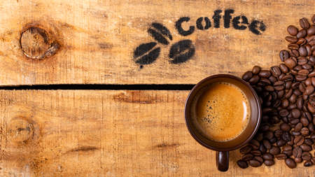 on a rough wooden box, a cup with creamy coffee and roasted coffee beansの写真素材