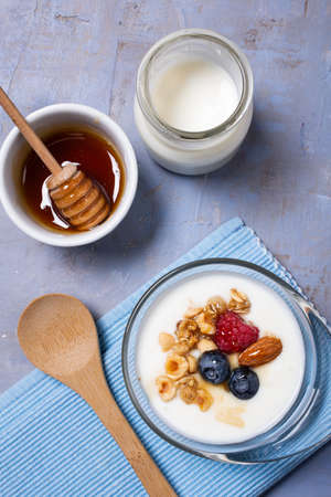 Healthy breakfast. Glass bowl with organic yogurt, fresh raspberries and blueberries, nuts and honey, on a textured wooden backgroundの写真素材