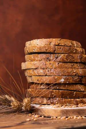 in the foreground slices of wholemeal bread with seeds and cereals and ears of wheatの写真素材
