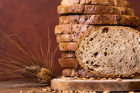 in the foreground slices of wholemeal bread with seeds and cereals and ears of wheatの写真素材