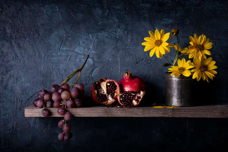 on the rustic wooden shelf, a bunch of grapes, pomegranates and yellow Jerusalem artichoke flowers. Still lifeの写真素材