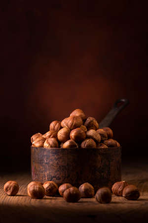 In the foreground, a group of shelled hazelnuts in an aged metal measuring cup against a dark backgroundの写真素材