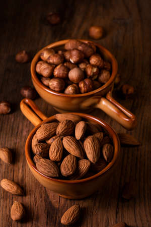 in the foreground two bowls with shelled hazelnuts and almonds on a rustic wooden backgroundの写真素材