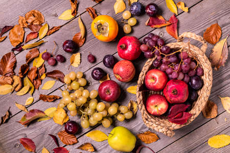 on a rustic wooden background a harvest of seasonal fruit and autumn colored dry leaves.の写真素材
