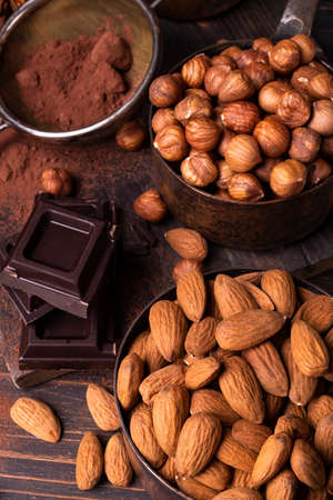 Still life. in the foreground, vintage metal measuring spoons with shelled hazelnuts and almonds, cocoa powder and pieces of dark chocolate.の写真素材