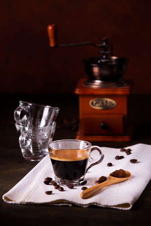 in the foreground, hot coffee in a glass cup, and a wooden spoon with raw cane sugar, in the background a vintage coffee grinder. still lifeの写真素材