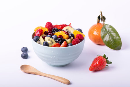 Fresh mixed fruit salad in a bowl with a wooden spoon in the foreground. White backgroundの写真素材