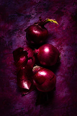 Fresh red onions on a rough background with shades of red and purple, top view. Still lifeの写真素材