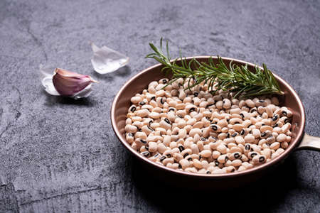 Dried cowpeas in copper pan with garlic and rosemary on black textured backgroundの写真素材