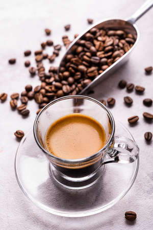 in the foreground a transparent glass cup with Italian espresso coffee, in the background roasted coffee beansの写真素材
