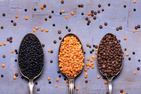 In the foreground, top view, on a colored textured background, three spoons with dried red and black...