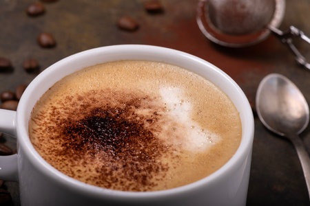 in the foreground, in a white ceramic cup, a frothy cappuccino dusted with cocoa powderの写真素材