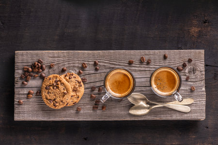 On the rustic wooden table, in the foreground, two fragrant coffees in glass cups, and chocolate chip cookiesの写真素材