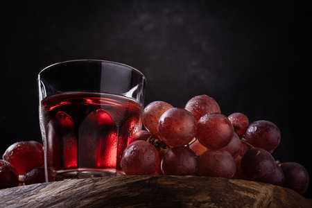 The side light illuminates a bunch of red grapes and a glass of wine in the foregroundの写真素材