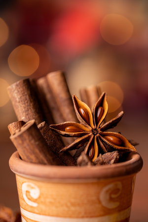 In the foreground, in a colored earthenware jar, some cinnamon sticks and an anise star, lights on a bokeh background. Still lifeの写真素材