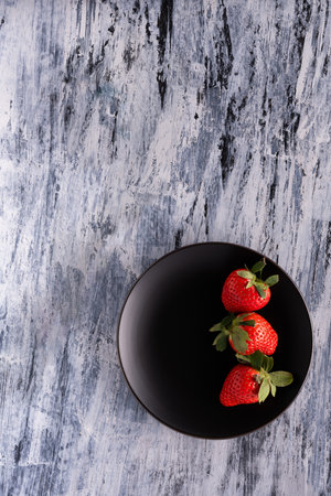 on a rustic background, a black plate with three red strawberries. Still lifeの写真素材