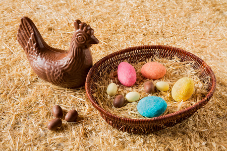 Easter chocolate chicken over the straw and some eggs in a basketの写真素材