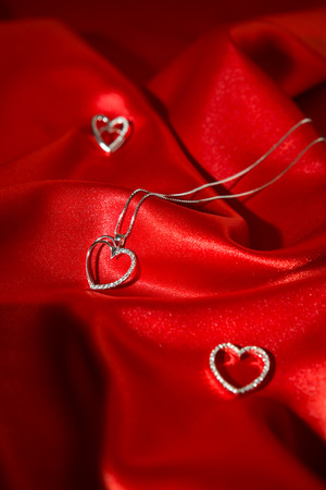 Silver heart pendants over a red satin backgroundの写真素材