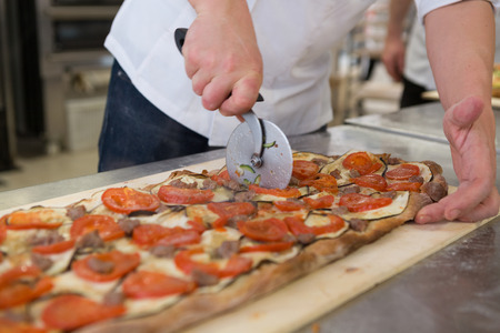 Pizza maker cutting focaccia romana with tomatoes, aubergine and sausageの写真素材