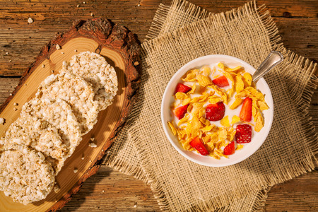 Continental breakfast with cornflakes, strawberries, rice crackers and a cup of milk seen from above