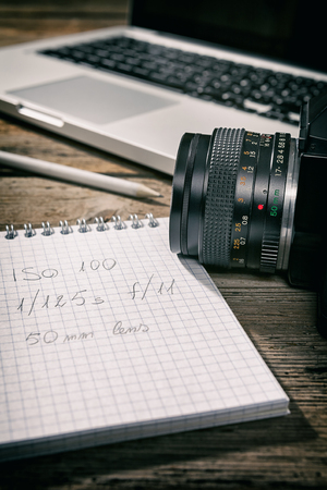 Closeup of a written notebook and a camera with a laptop on backgroundの写真素材