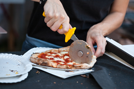 Pizza maker cutting a pizza margherita in slices ready to takeawayの写真素材