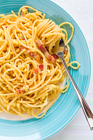 Closeup of spaghetti carbonara on fork with egg, smoked bacon and cheese over a table seen from aboveの写真素材