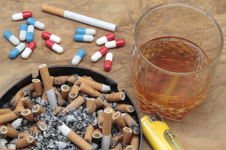 cigars on a ashtray full of ash, pills and whiskey on a wooden tableの写真素材