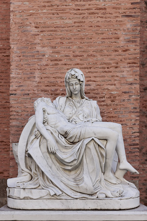 vertical image of a replica of Miguel Angel famous sculpture the Pieta at Adolfo Suarez park of Torrejon de Ardoz, madrid, spain with a wall of bricks as backgroundのeditorial素材