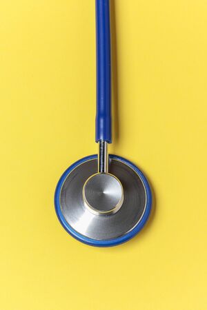 vertical view of the bell of a blue stethoscope on foreground isolated on yellow backgroundの写真素材