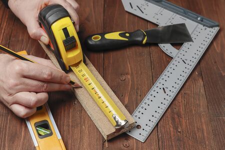 horizontal view from above of two hands using a pencil and a flexometer to measure the lenght of a wood strip on a set with others DIY toolsの写真素材