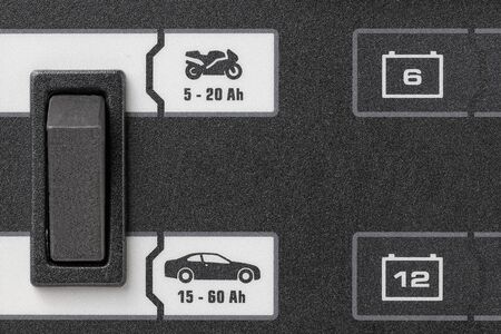 horizontal view in foreground of part of a  panel of a battery charger with motorcycle and car...